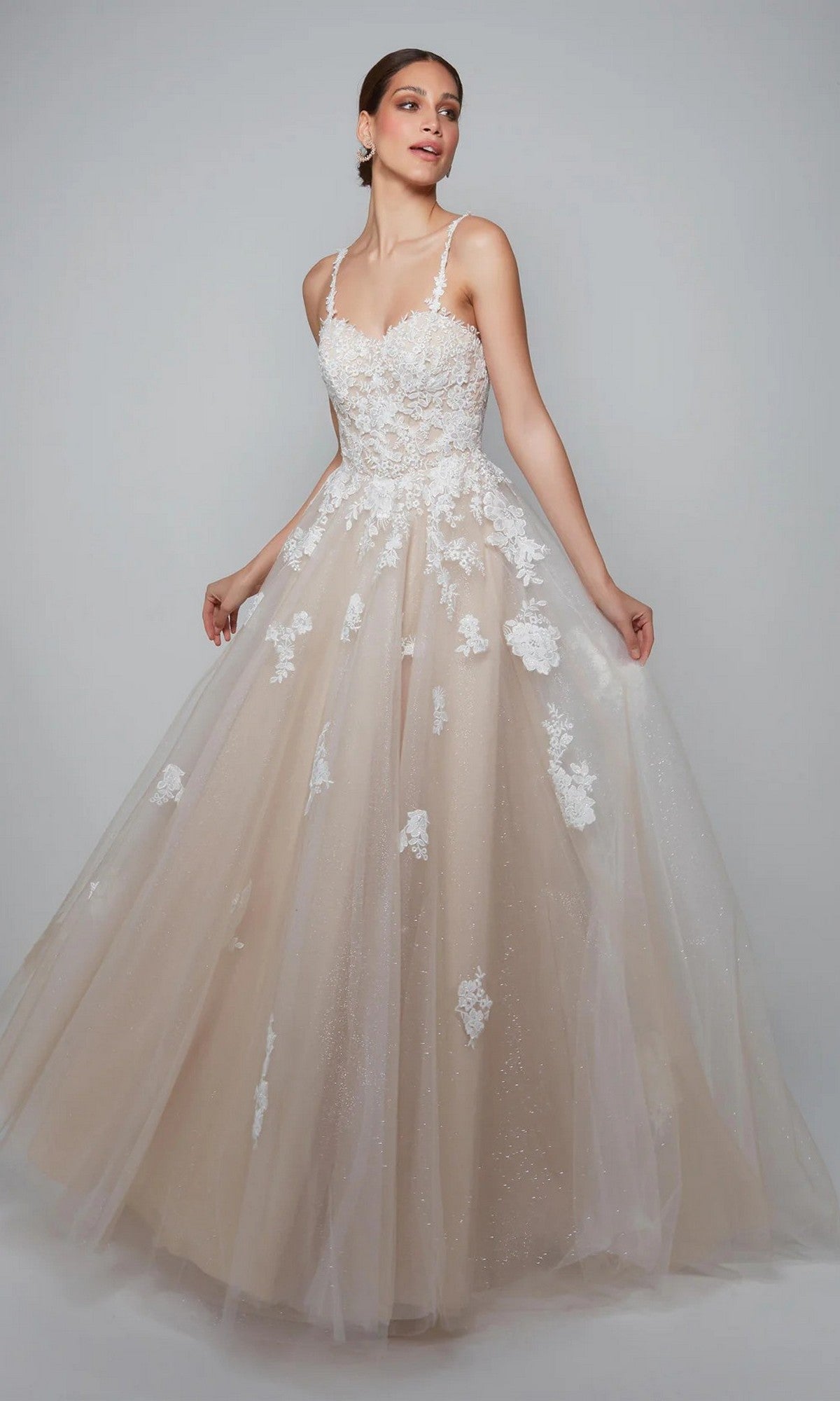 A woman poses in the Alyce 7084 Long White Dress in Ivory/Lt Latte, featuring a sleeveless fitted lace bodice with lace appliques and a full tulle skirt adorned with floral details.